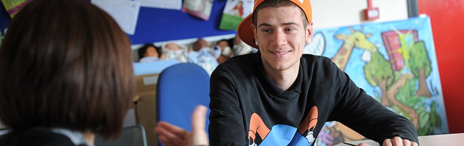 Male student talks to tutor sat in classroom